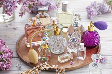 Photo of Bottles of perfumes, accessories and lilac flowers on white wooden table