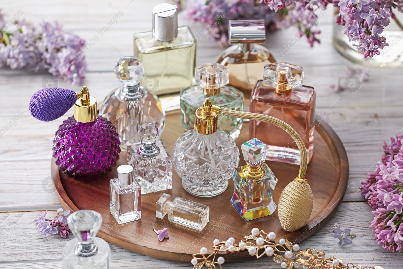 Bottles of perfumes, accessories and lilac flowers on white wooden table Photo of Bottles of perfumes, accessories and lilac flowers on white wooden table