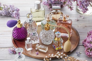 Photo of Bottles of perfumes, accessories and lilac flowers on white wooden table