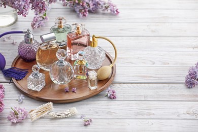 Photo of Bottles of perfumes, accessories and lilac flowers on white wooden table. Space for text