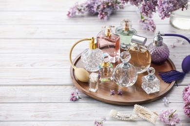 Photo of Bottles of perfumes, accessories and lilac flowers on white wooden table. Space for text