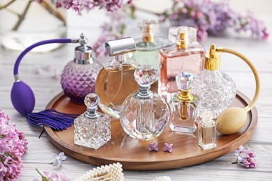 Photo of Bottles of perfumes, accessories and lilac flowers on white wooden table, closeup