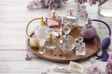 Photo of Bottles of perfumes, accessories and lilac flowers on white wooden table
