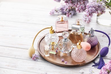 Photo of Bottles of perfumes and lilac flowers on white wooden table. Space for text