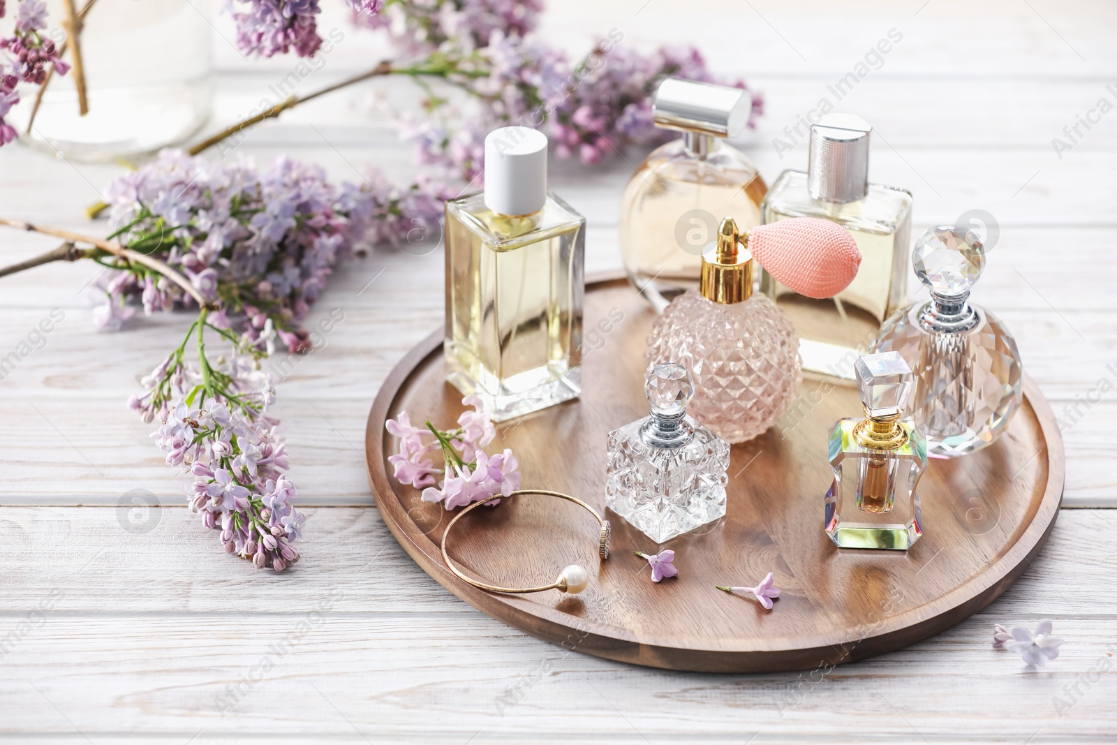 Bottles of perfumes and lilac flowers on white wooden table Photo of Bottles of perfumes and lilac flowers on white wooden table