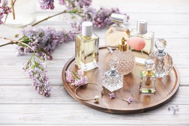 Photo of Bottles of perfumes and lilac flowers on white wooden table