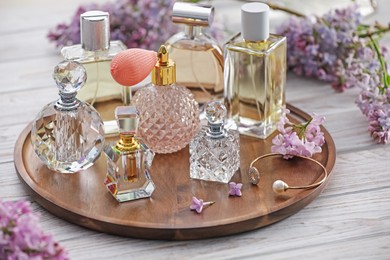 Photo of Bottles of perfumes and lilac flowers on white wooden table, closeup