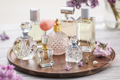 Photo of Bottles of perfumes and lilac flowers on white wooden table, closeup