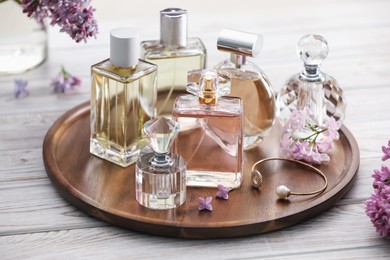 Photo of Bottles of perfumes and lilac flowers on white wooden table, closeup