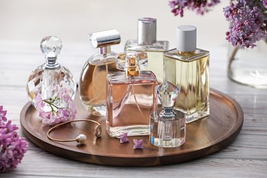 Photo of Bottles of perfumes and lilac flowers on white wooden table, closeup