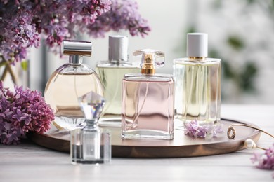 Photo of Bottles of perfumes and lilac flowers on white wooden table, closeup