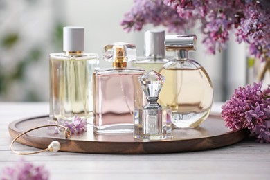Photo of Bottles of perfumes and lilac flowers on white wooden table, closeup