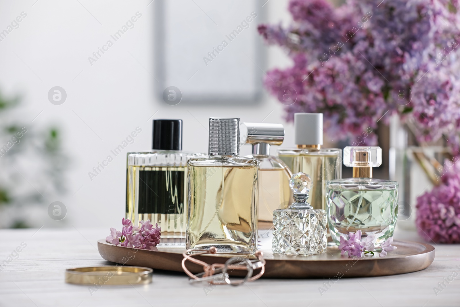Bottles of perfumes and lilac flowers on white wooden table Photo of Bottles of perfumes and lilac flowers on white wooden table