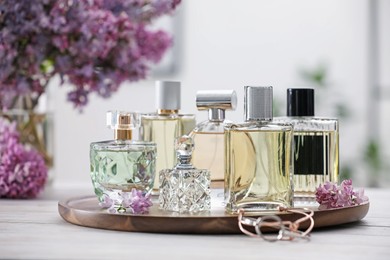 Photo of Bottles of perfumes and lilac flowers on white wooden table