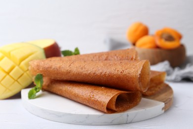 Photo of Delicious fruit leather rolls, mint, mango and apricots on white table, closeup