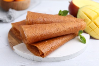 Photo of Delicious fruit leather rolls, mint and mango on white table, closeup