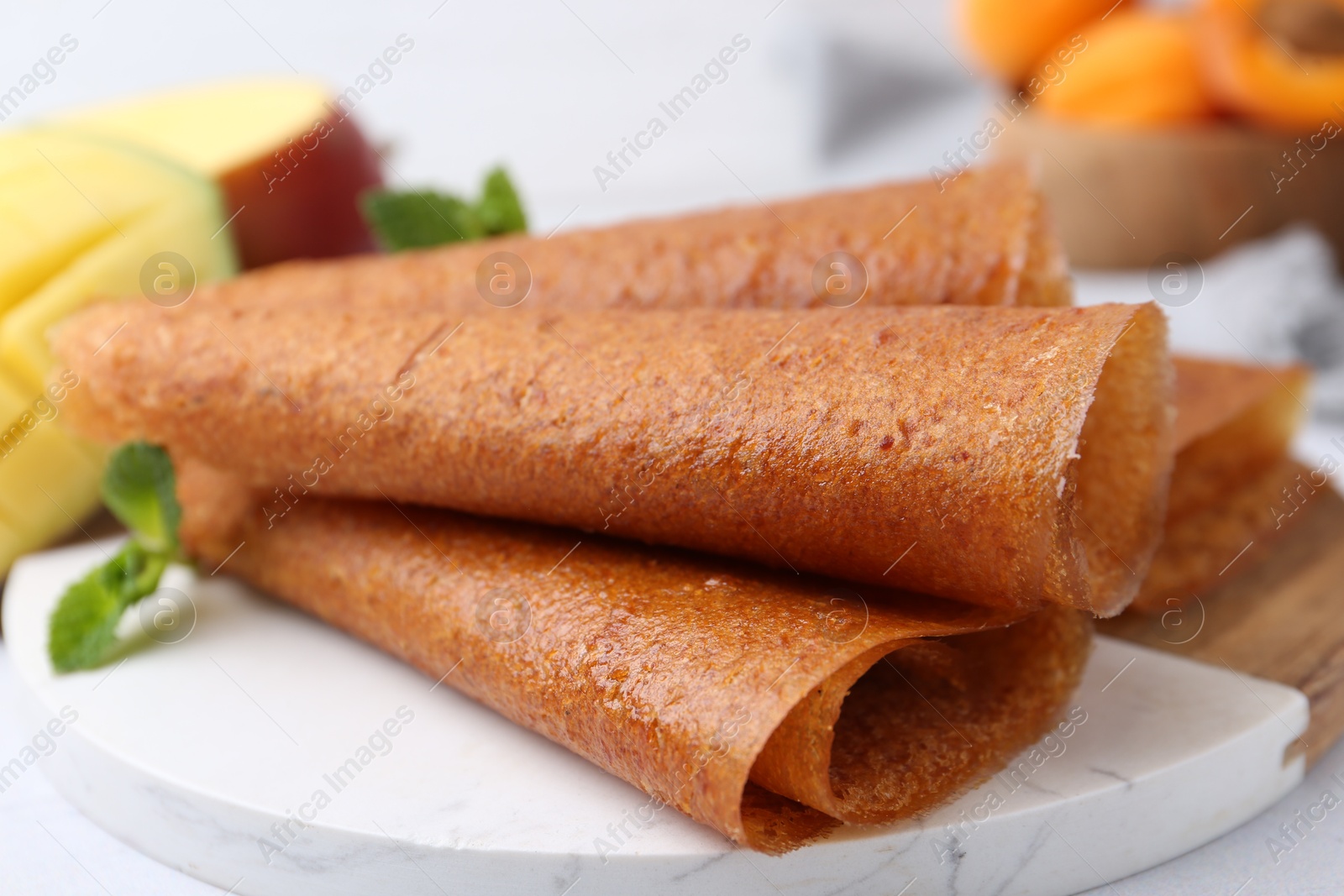 Delicious fruit leather rolls, mint and mango on table, closeup Photo of Delicious fruit leather rolls, mint and mango on table, closeup