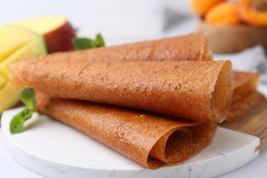 Photo of Delicious fruit leather rolls, mint and mango on table, closeup