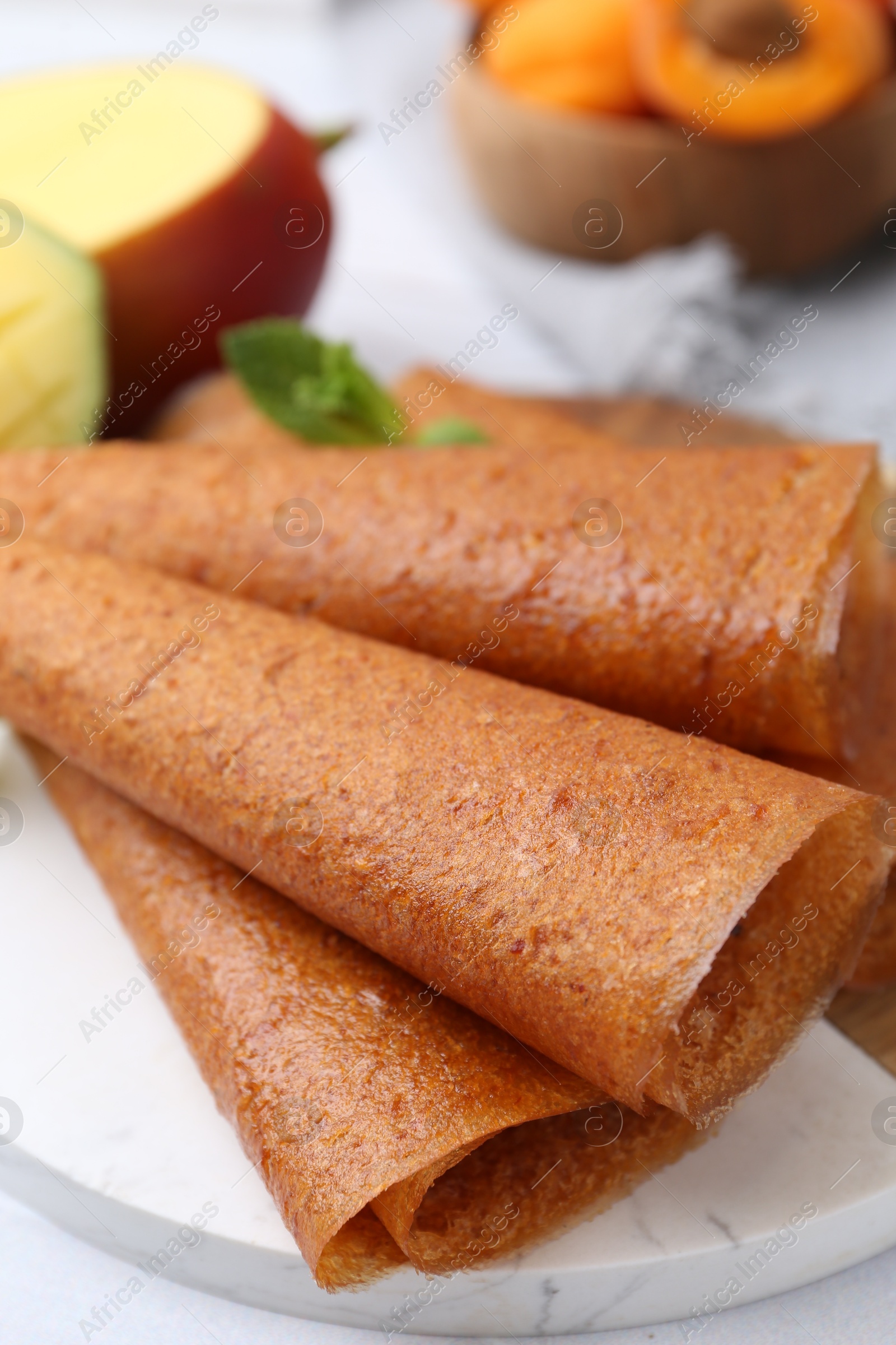 Delicious fruit leather rolls, mint, mango and apricots on table, closeup Photo of Delicious fruit leather rolls, mint, mango and apricots on table, closeup