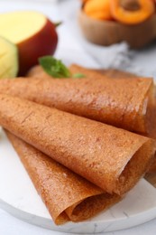 Photo of Delicious fruit leather rolls, mint, mango and apricots on table, closeup