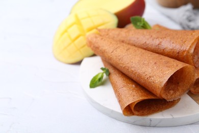 Photo of Delicious fruit leather rolls, mint and mango on white table, closeup. Space for text