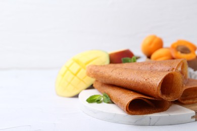 Photo of Delicious fruit leather rolls, mint, mango and apricots on white table, closeup. Space for text