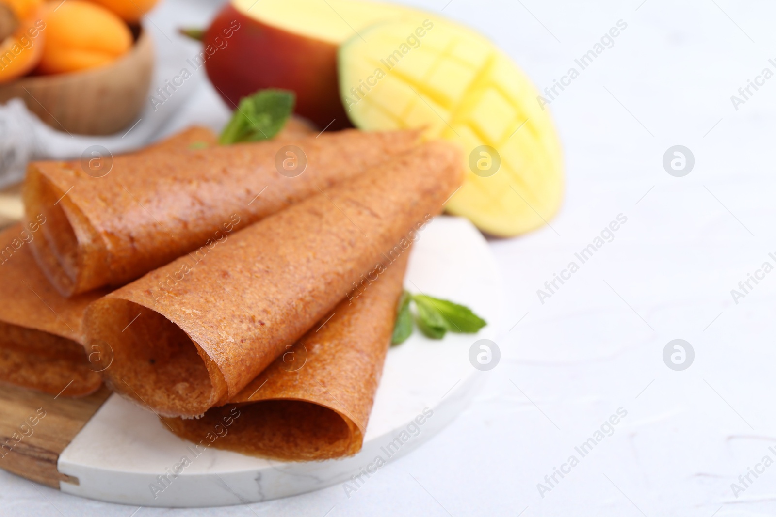 Delicious fruit leather rolls, mint, mango and apricots on white table, closeup. Space for text Photo of Delicious fruit leather rolls, mint, mango and apricots on white table, closeup. Space for text