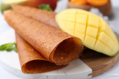 Photo of Delicious fruit leather rolls, mint and mango on table, closeup