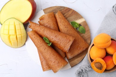 Photo of Delicious fruit leather rolls, mint, mango and apricots on white table, flat lay