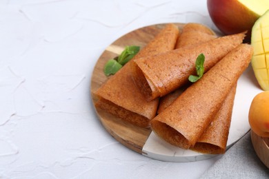 Photo of Delicious fruit leather rolls, mint and mango on white table, closeup. Space for text
