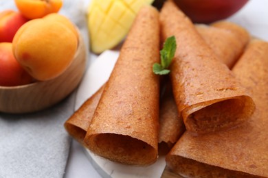 Photo of Delicious fruit leather rolls, mint, mango and apricots on table, closeup