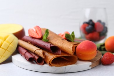 Photo of Delicious fruit leather rolls, mint, mango and berries on light table, closeup