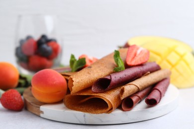 Photo of Delicious fruit leather rolls, mint, apricots and berries on light table, closeup
