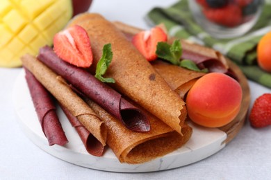Photo of Delicious fruit leather rolls, mint, apricot, mango and strawberry on light table, closeup