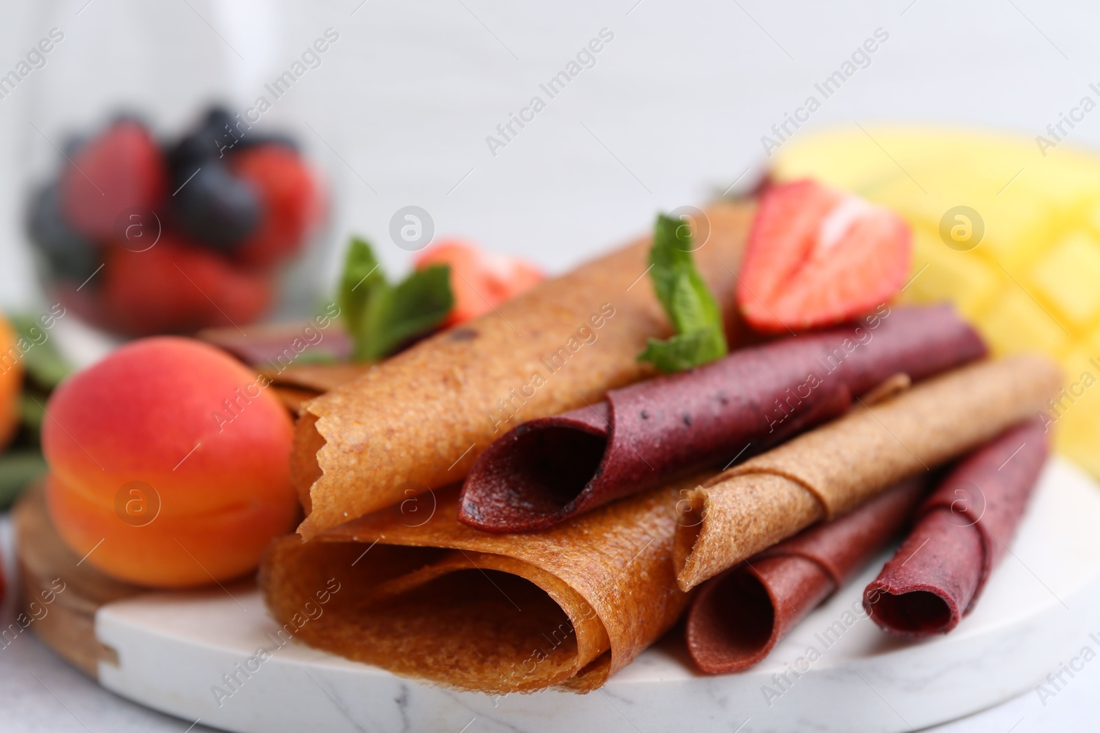 Delicious fruit leather rolls, mint, apricot and strawberry on table, closeup Photo of Delicious fruit leather rolls, mint, apricot and strawberry on table, closeup