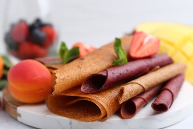 Photo of Delicious fruit leather rolls, mint, apricot and strawberry on table, closeup