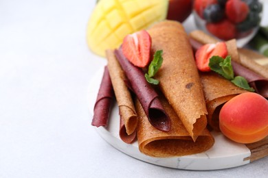 Photo of Delicious fruit leather rolls, mint, mango and berries on light table, closeup. Space for text