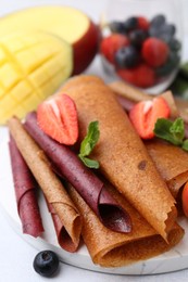 Photo of Delicious fruit leather rolls, mint, mango and berries on light table, closeup