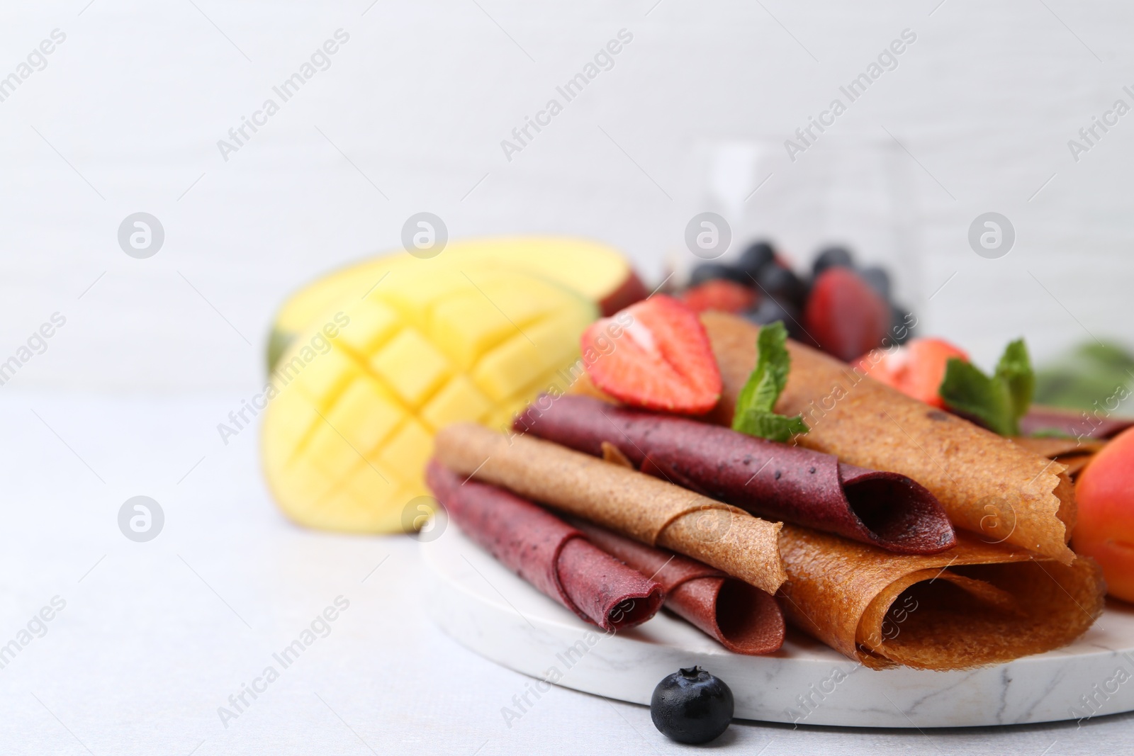 Delicious fruit leather rolls, mint, mango and berries on light table, closeup. Space for text Photo of Delicious fruit leather rolls, mint, mango and berries on light table, closeup. Space for text