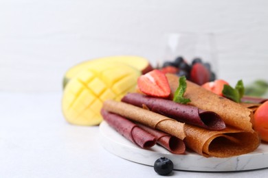 Photo of Delicious fruit leather rolls, mint, mango and berries on light table, closeup. Space for text