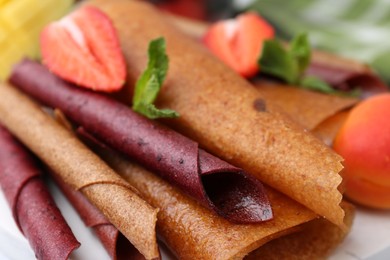 Photo of Delicious fruit leather rolls, mint and strawberry on table, closeup