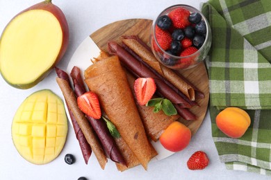 Photo of Delicious fruit leather rolls, mint, mango, apricots and berries on light table, flat lay