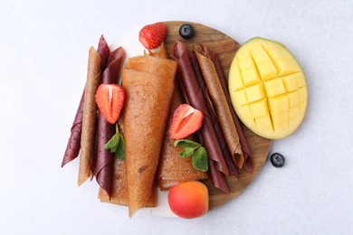 Photo of Delicious fruit leather rolls, mint, mango, apricot and berries on light table, flat lay