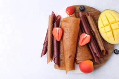 Photo of Delicious fruit leather rolls, mango, apricot and berries on light table, flat lay. Space for text