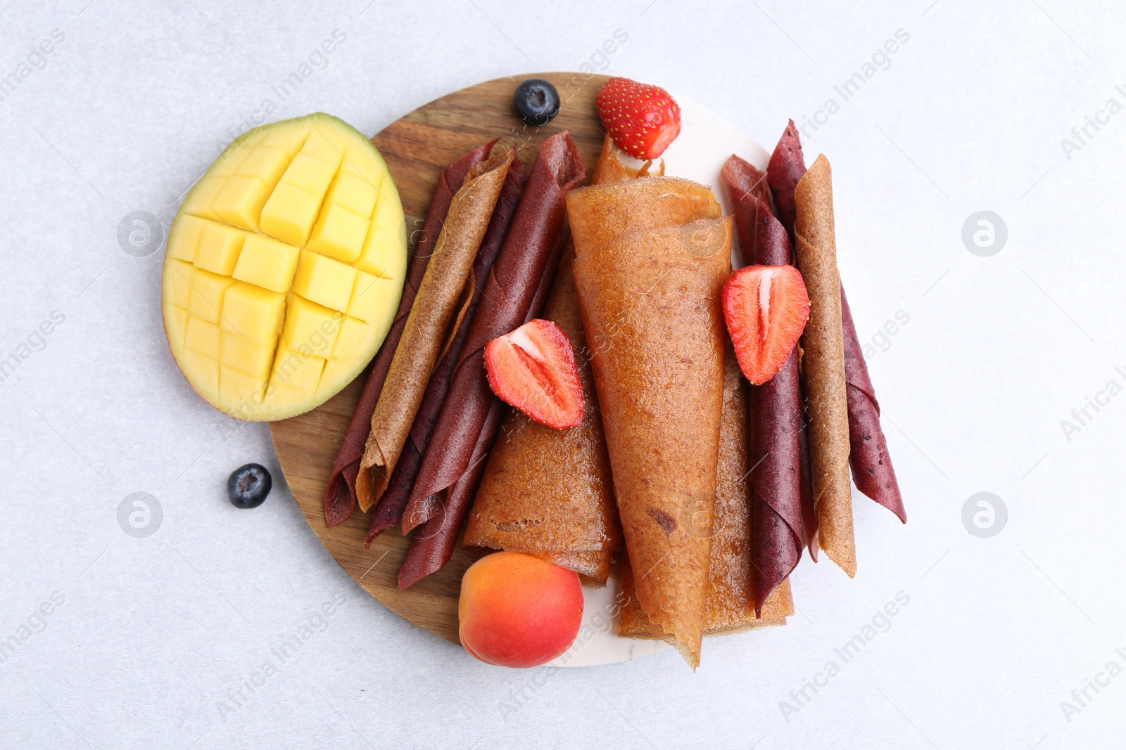 Delicious fruit leather rolls, mango, apricot and berries on light table, flat lay Photo of Delicious fruit leather rolls, mango, apricot and berries on light table, flat lay