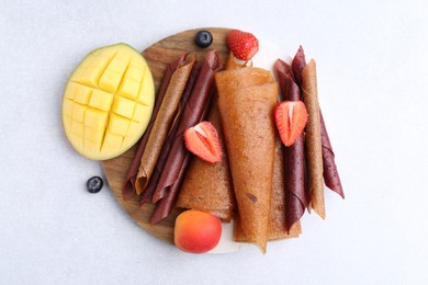 Photo of Delicious fruit leather rolls, mango, apricot and berries on light table, flat lay
