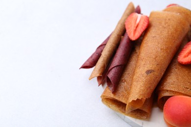 Photo of Delicious fruit leather rolls, strawberry and apricot on light table, closeup. Space for text