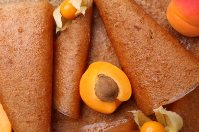 Photo of Delicious fruit leather rolls, apricots and physalis as background, top view