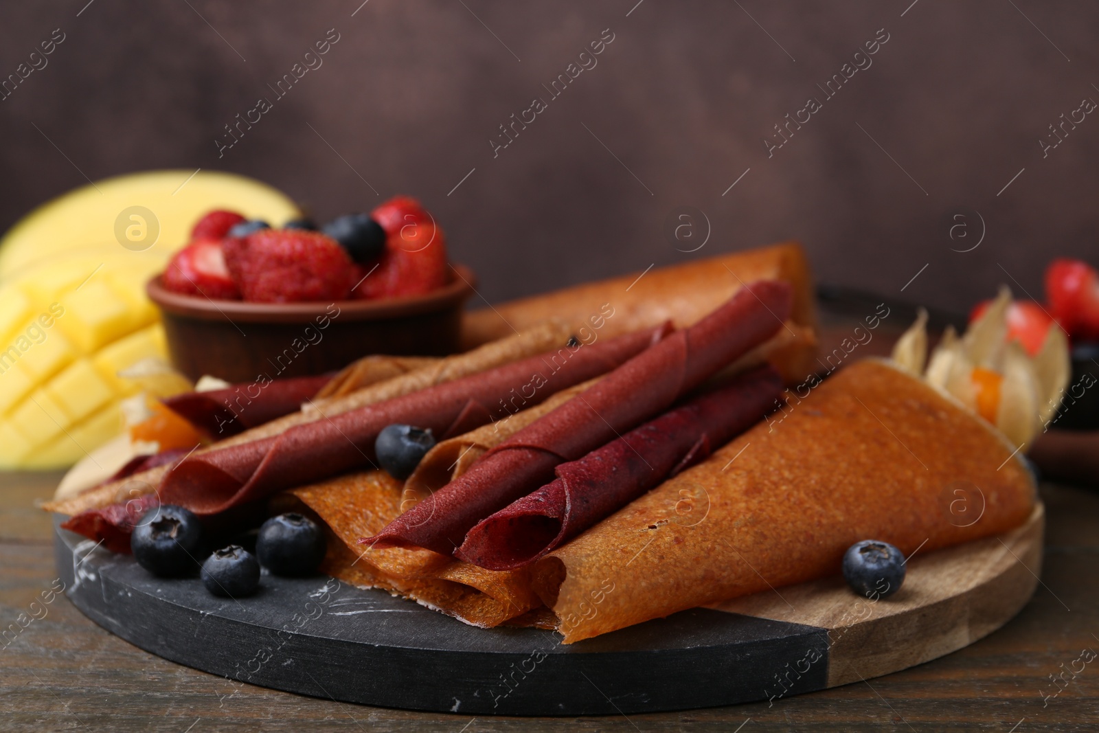 Delicious fruit leather rolls and berries on wooden table, closeup Photo of Delicious fruit leather rolls and berries on wooden table, closeup