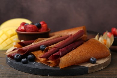 Photo of Delicious fruit leather rolls and berries on wooden table, closeup